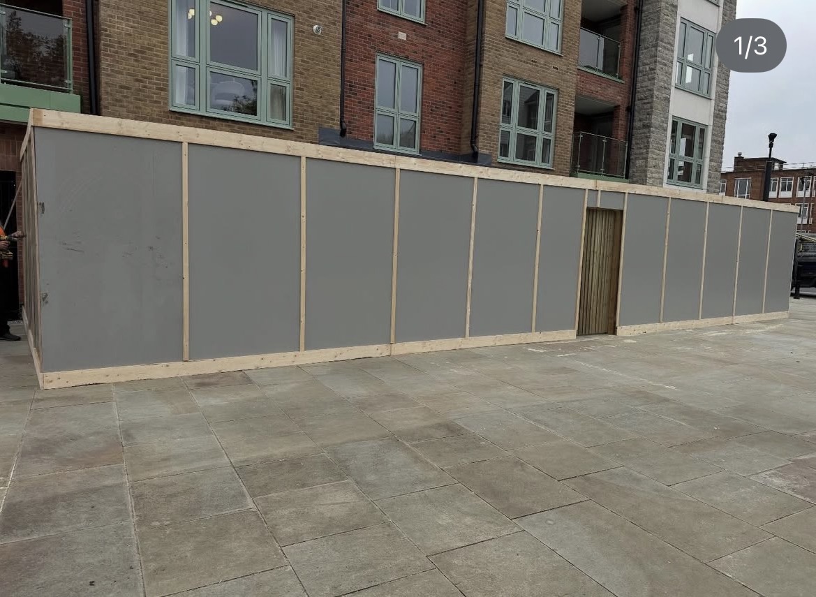 Grey panel site hoarding with timber gate access